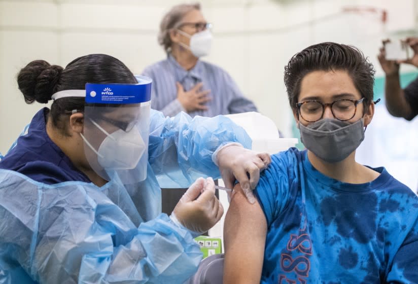 Eagle Rock, CA - August 30: Registered Nurse Priscilla V., left, gives a Pfizer-BioNTech vaccine shot to Dean Iida, 17, a senior at Eagle Rock High School, as Los Angeles County Board of Supervisors Chair Hilda Solis, Interim Superintendent Megan K. Reilly, School Board members Kelly Gonez and Jackie Goldberg and special guests visit Los Angeles Unified School-based mobile vaccination clinics at Eagle Rock High School on Monday, Aug. 30, 2021 in Eagle Rock, CA. All employees in the Los Angeles Unified School District must be vaccinated against COVID-19 by Oct. 15, an order that puts it at the forefront of school systems across the country that are mandating strict coronavirus safety measures for employees and students. (Allen J. Schaben / Los Angeles Times)