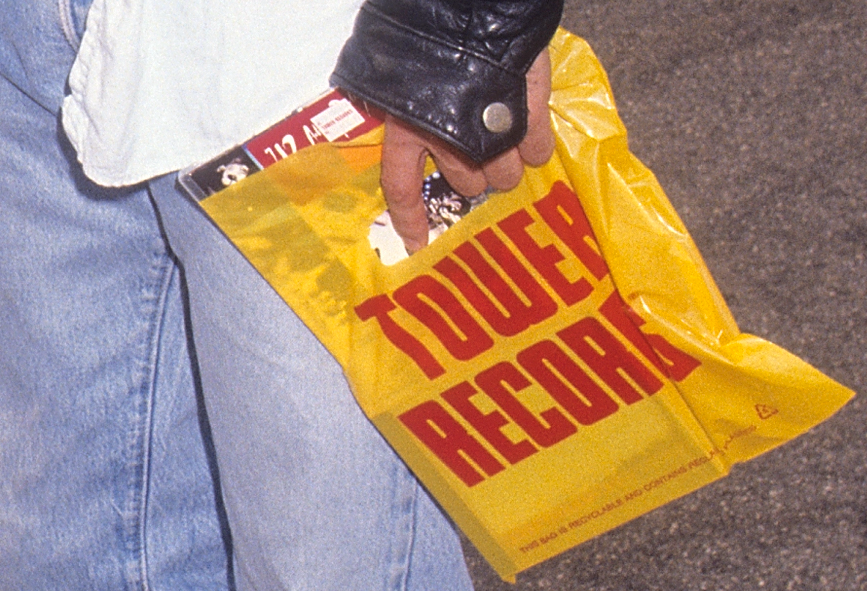 Person holding a Tower Records bag, denim attire, hint of a black leather glove