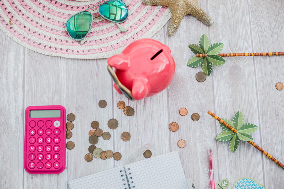 Piggy bank on a desk surrounded by money and a pink calculator.