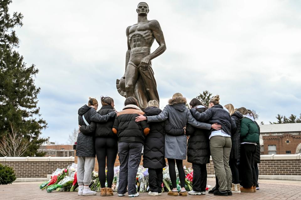 A group hugs after leaving flowers at the Sparty statue on the one-year anniversary of the mass shooting on Tuesday, Feb. 13, 2024, on campus in East Lansing.