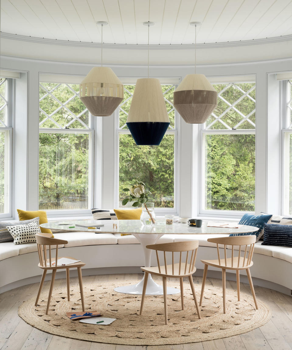 Dining area with bay window and round shapes of large glass cafe table, hessian rug and window seating with three lanterns above