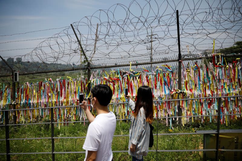 A couple takes a picture of a military fence decorated with ribbons bearing messages wishing for reunification, near the the demilitarized zone (DMZ) separating the two Koreas, in Paju