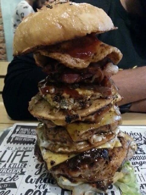 A massive burger with multiple beef patties, slices of cheese, bacon and sauce on a bun