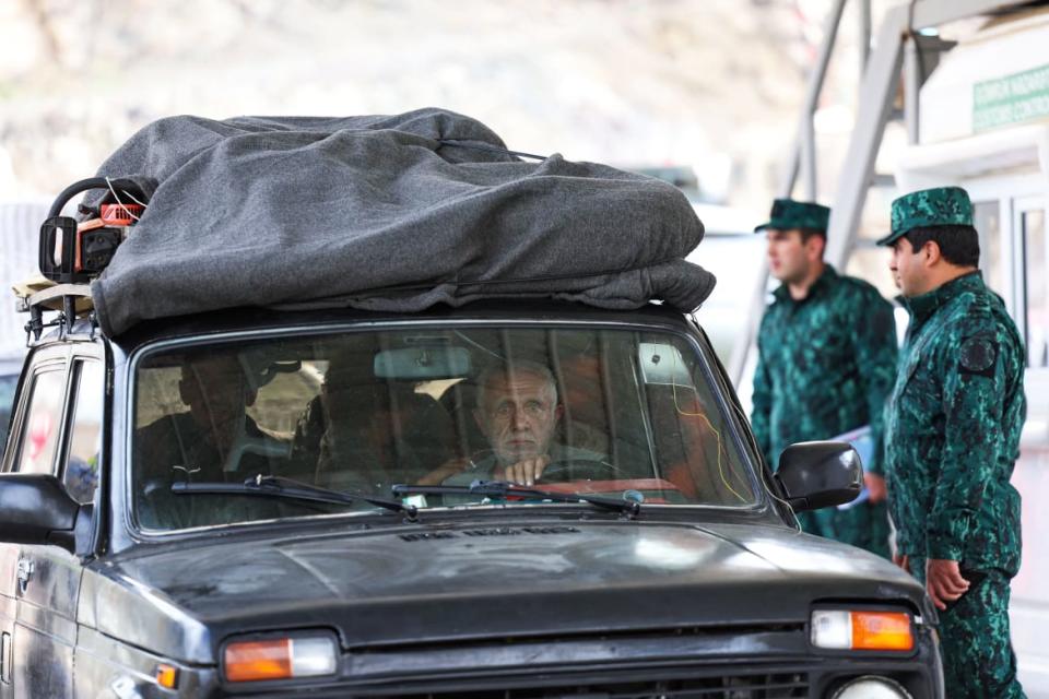 A photograph of Azerbaijan soldiers control a car, as refugees wait in their car to leave Karabakh for Armenia, at the in Lachin checkpoint, on September 26, 2023.