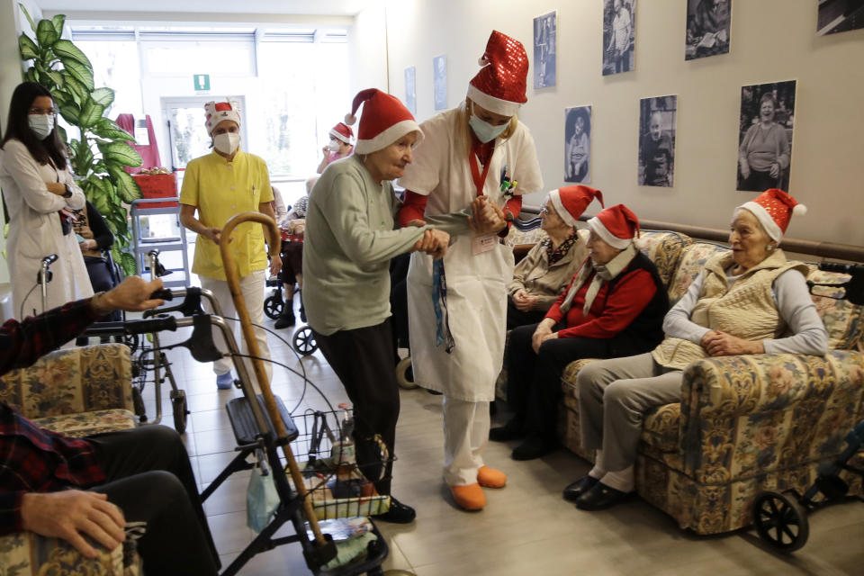 Director Maria Giulia Madaschi, right, takes by the hand Pasqualina Ghilardi, 87, before talking via video call with Caterina Damiano, a donor unrelated to her, who bought and sent her a Christmas present through an organization dubbed "Santa's Grandchildren", at the Martino Zanchi nursing home in Alzano Lombardo, one of the area that most suffered the first wave of COVID-19, in northern Italy, Saturday, Dec. 19, 2020. (AP Photo/Luca Bruno)