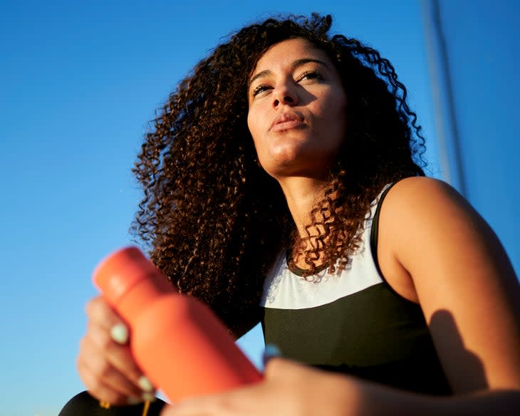 Young black female athlete with water bottle on sunny day; drinking enough water is key when running with a UTI