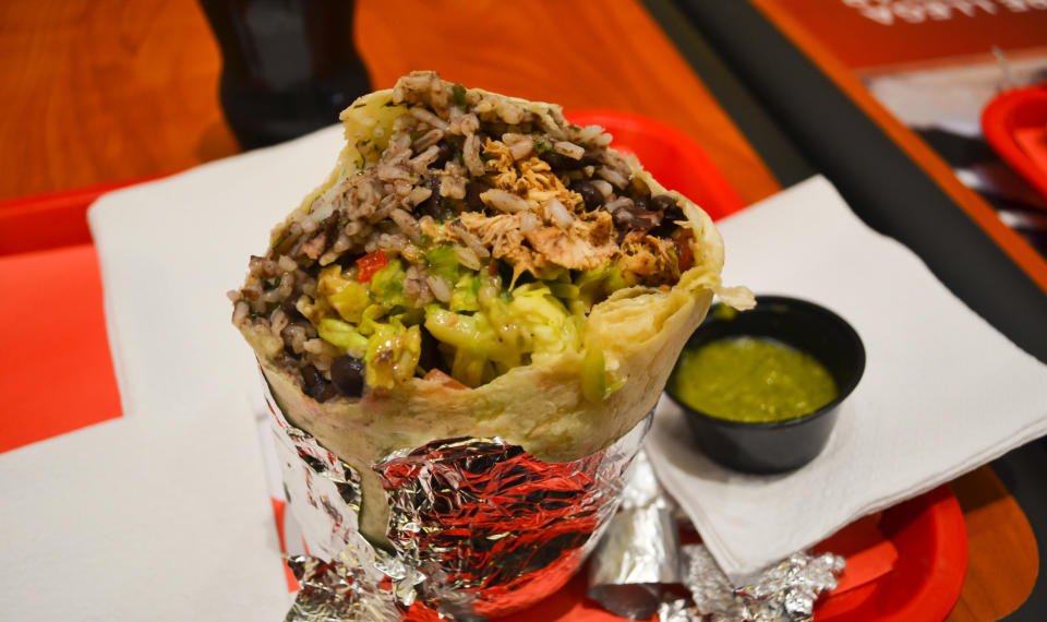 Burrito with meat, rice, bean and vegetables in aluminum foil.