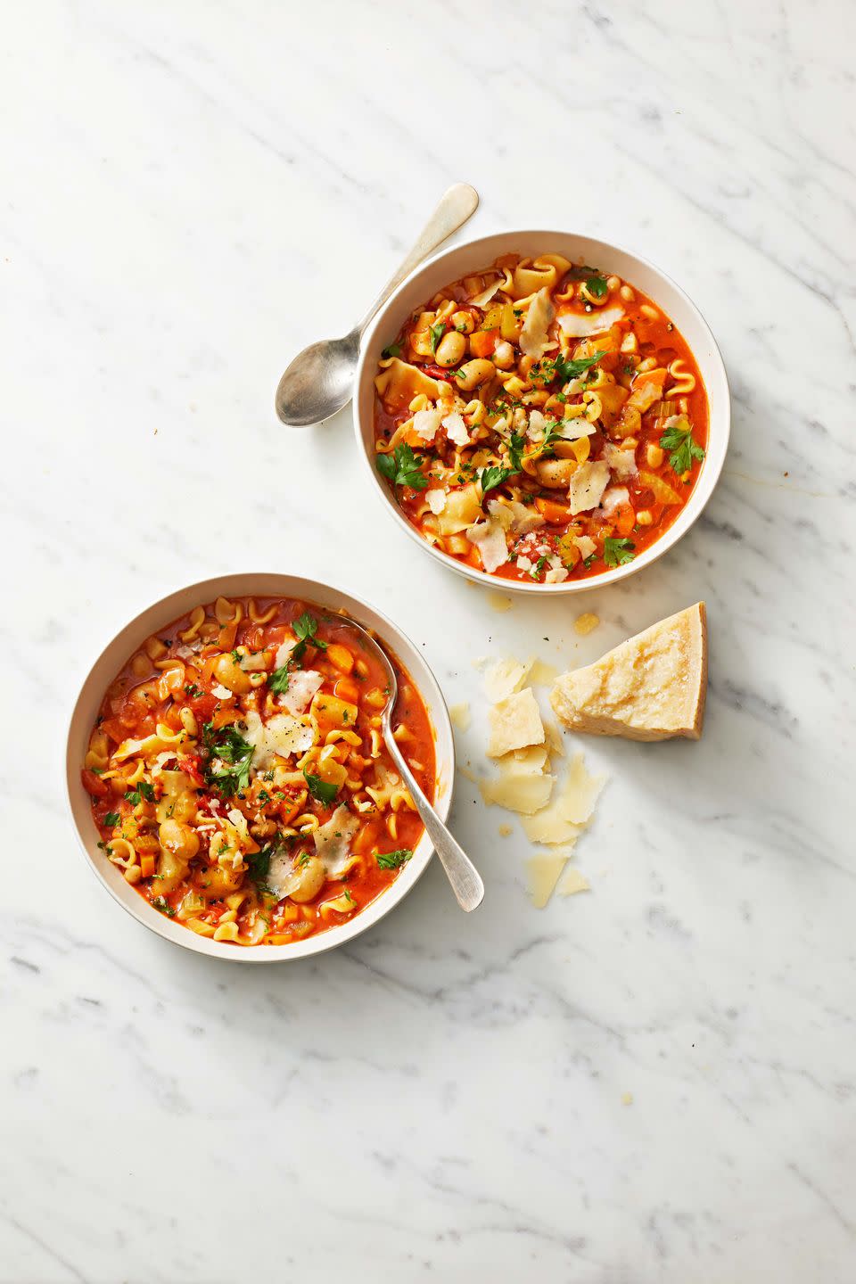 pasta e fagioli in a white bowl and a chunk of parmesan on the side