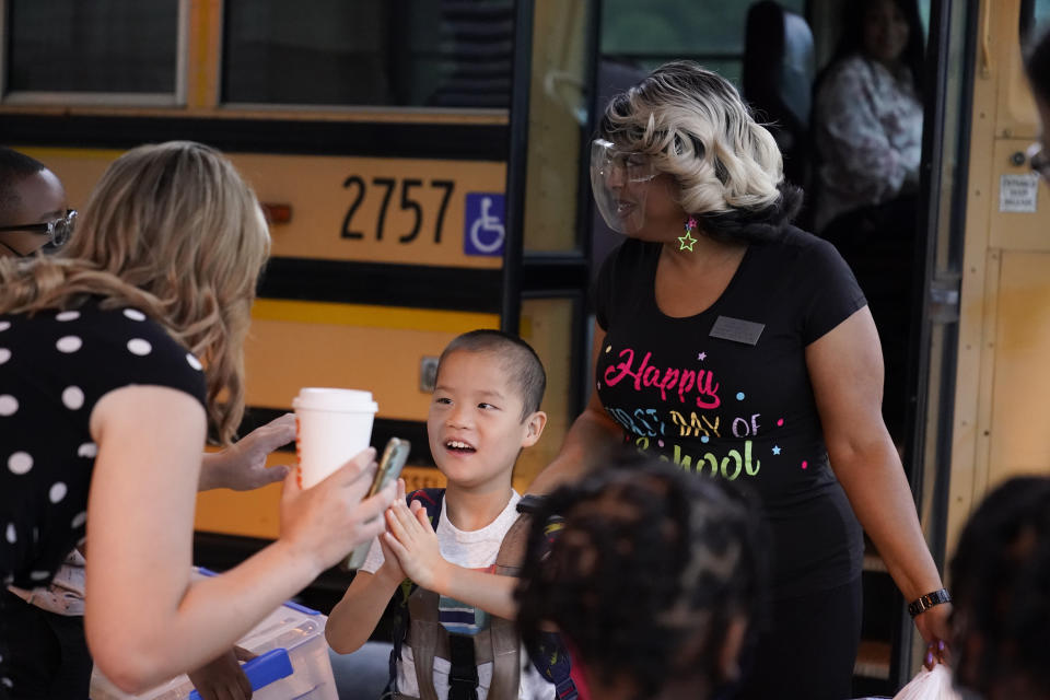 Teachers greet students when the arrive to school off the school bus at Tussahaw Elementary school on Wednesday, Aug. 4, 2021, in McDonough, Ga. Schools have begun reopening in the U.S. with most states leaving it up to local schools to decide whether to require masks. (AP Photo/Brynn Anderson)