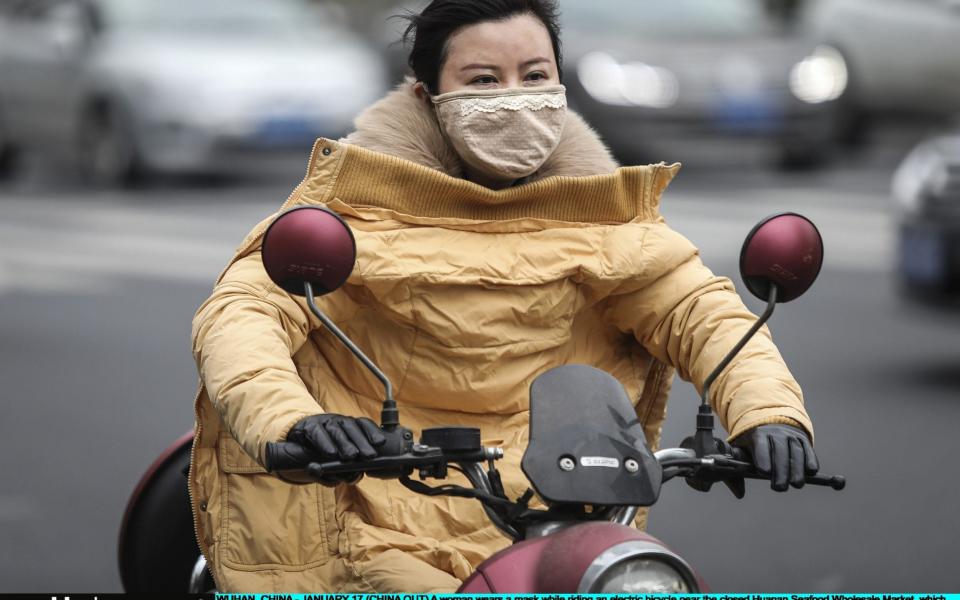  A woman wears a mask while riding an electric bicycle near the closed Huanan Seafood Wholesale Market, which has been linked to cases of coronavirus - Getty Images AsiaPac