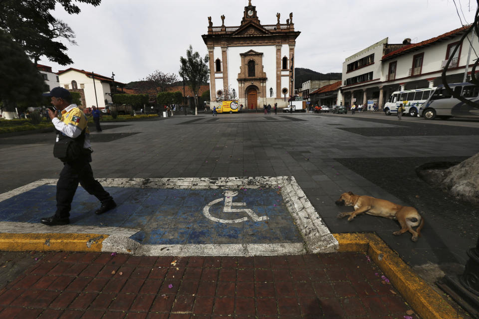 In this Feb. 6, 2020 photo, a dog naps on the city square as a police officer patrols in Uruapan, Michoacan state, Mexico. Uruapan, a city of about 340,000 people, is in Mexico's avocado belt, where violence has reached shocking proportions. In Uruapan, cartels are battling for territory and reports of killings are common, such as the gun massacre last week of three young boys, a teenager and five others at an arcade in what had been a relatively quiet neighborhood. (AP Photo/Marco Ugarte)