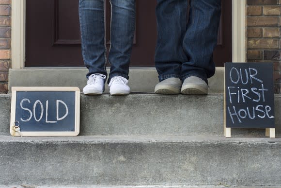 couples feet in front of house with our first house and sold sign