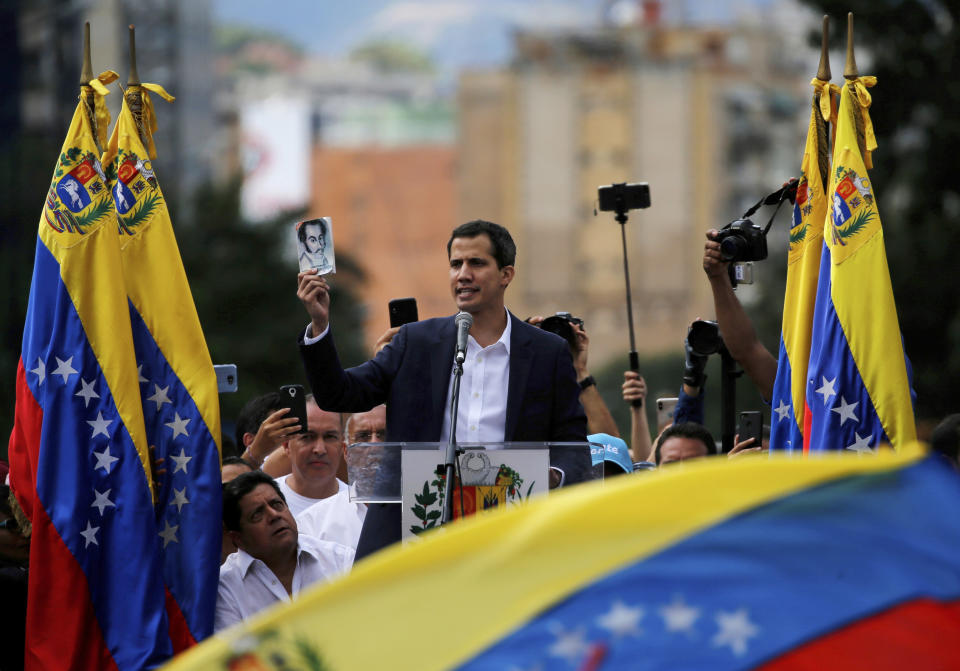 El líder opositor venezolano Juan Guaidó muestra una imagen del líder independentistas Simón Bolívar mientras se declara presidente "encargado" del país en un evento que demanda la renuncia del presidente Nicolás Maduro en Caracas, Venezuela, el miércoles 23 de enero de 2019. (AP Foto/Fernando Llano)