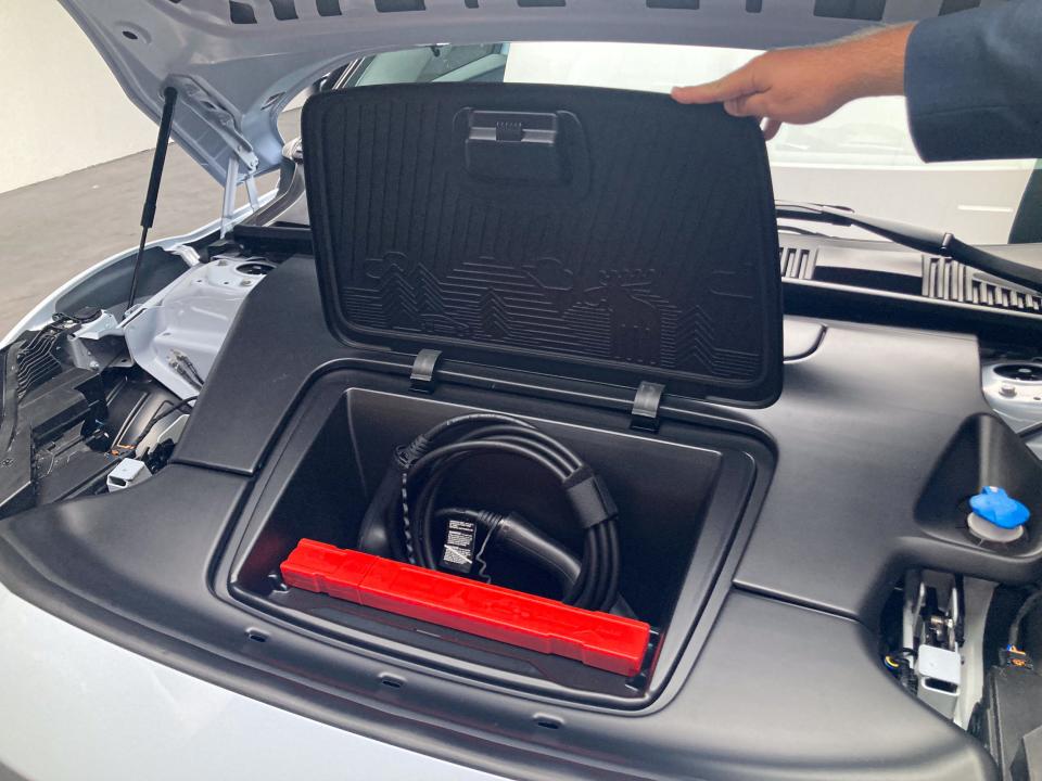 A hand opening the front bonnet of the Volvo EX30 to show a small storage space that has a charging cable.