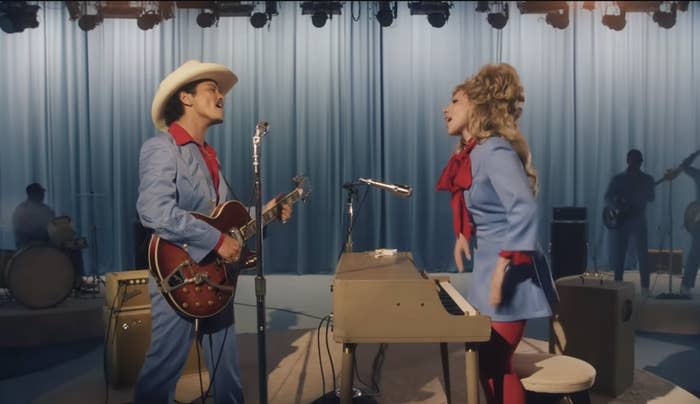 Orville Peck and Trixie Mattel appear on stage in retro-style suits, with Orville playing guitar and Trixie singing on a keyboard