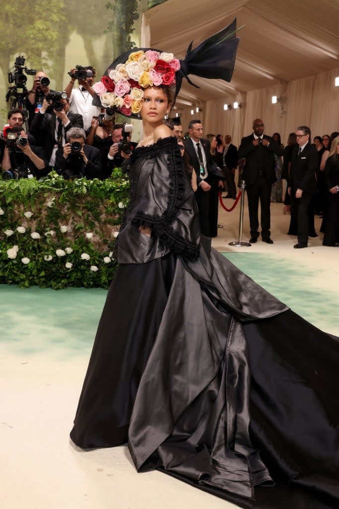 Zendaya in an elaborate floral headpiece and draped gown at an event with onlookers and cameras