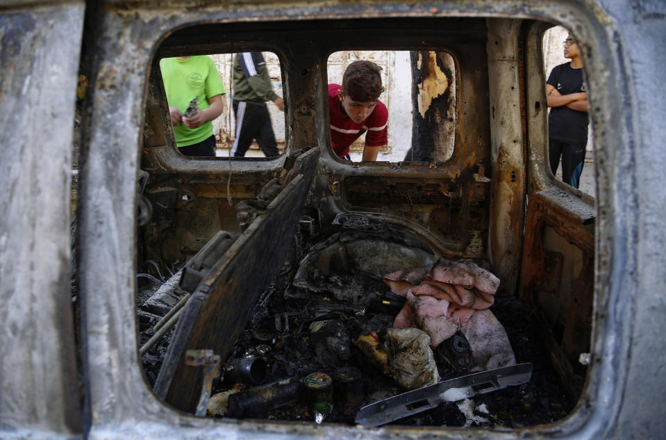 Palestinian kids look at a destroyed car after it was hit in an Israeli airstrike, in Gaza City, Wednesday, May 19, 2021. (AP Photo/Hatem Moussa)