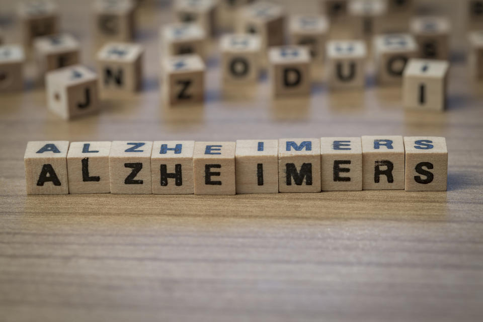 "Alzheimers" spelled in wooden blocks with more wooden blocks with letters on them in the background.