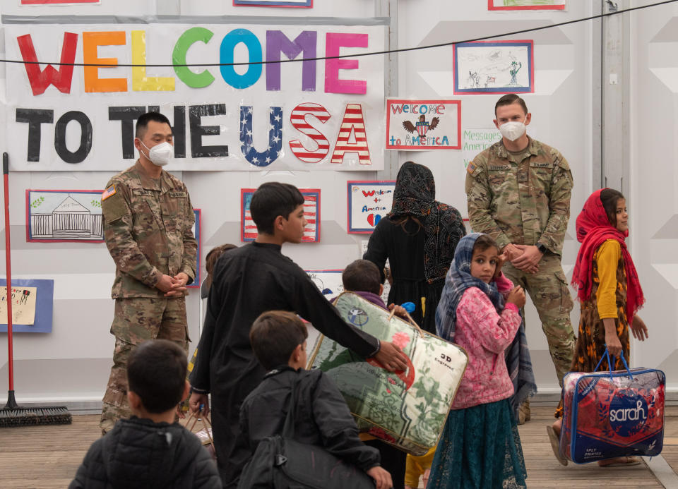 Afghan families walk through the waiting area for departure to the U.S. On the wall of the tent is written 