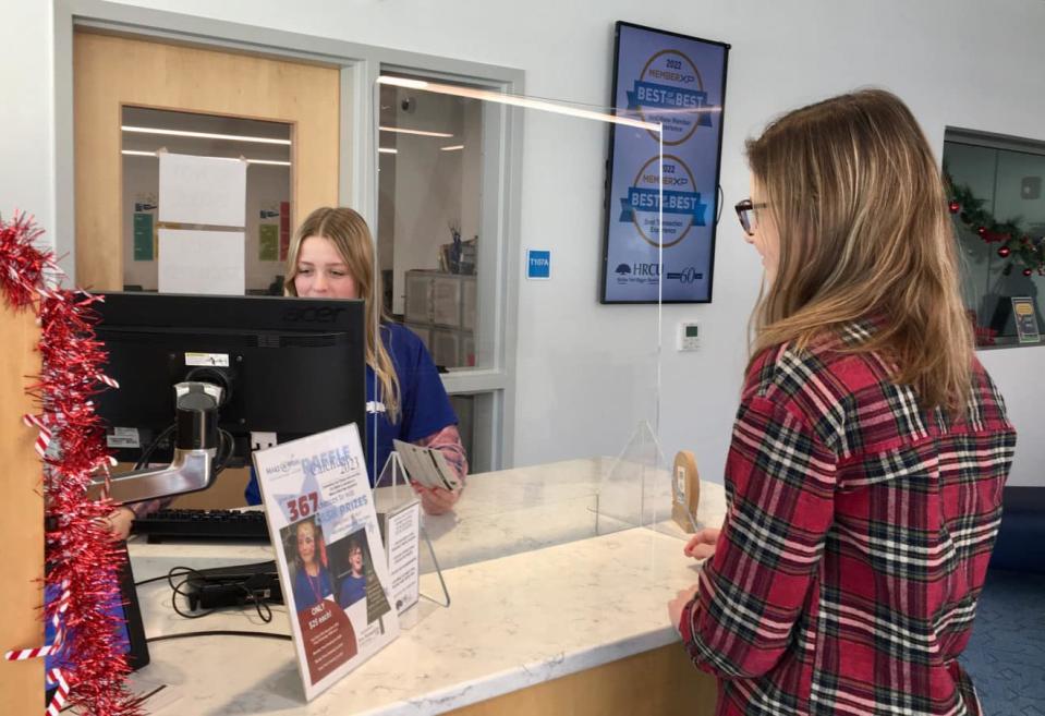 An intern from the R.W. Creteau Regional Technology Center helps another Spaulding High School student with a banking transaction at the HRCU (Holy Rosary Credit Union) branch inside the Technology Center.