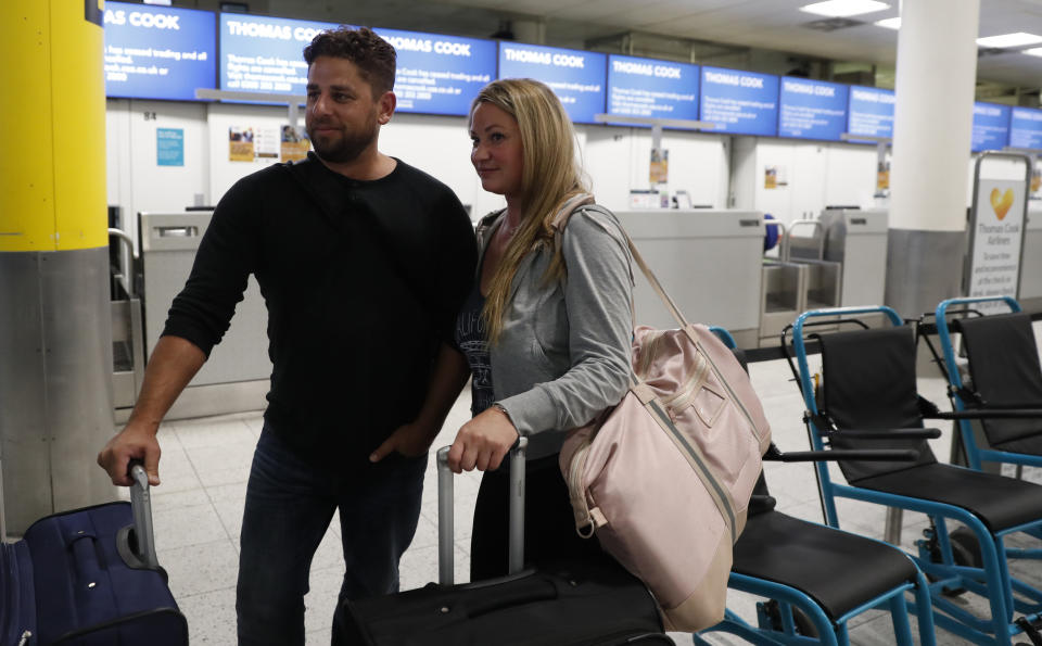 John Garret and Ajouline Chaffee from Boston Ma., who were supposed to be flying to Malta, speak to the media near the empty Thomas Cook check in desks in Gatwick Airport, England Monday, Sept. 23, 2019. British tour company Thomas Cook collapsed early Monday after failing to secure emergency funding, leaving tens of thousands of vacationers stranded abroad. (AP Photo/Alastair Grant)