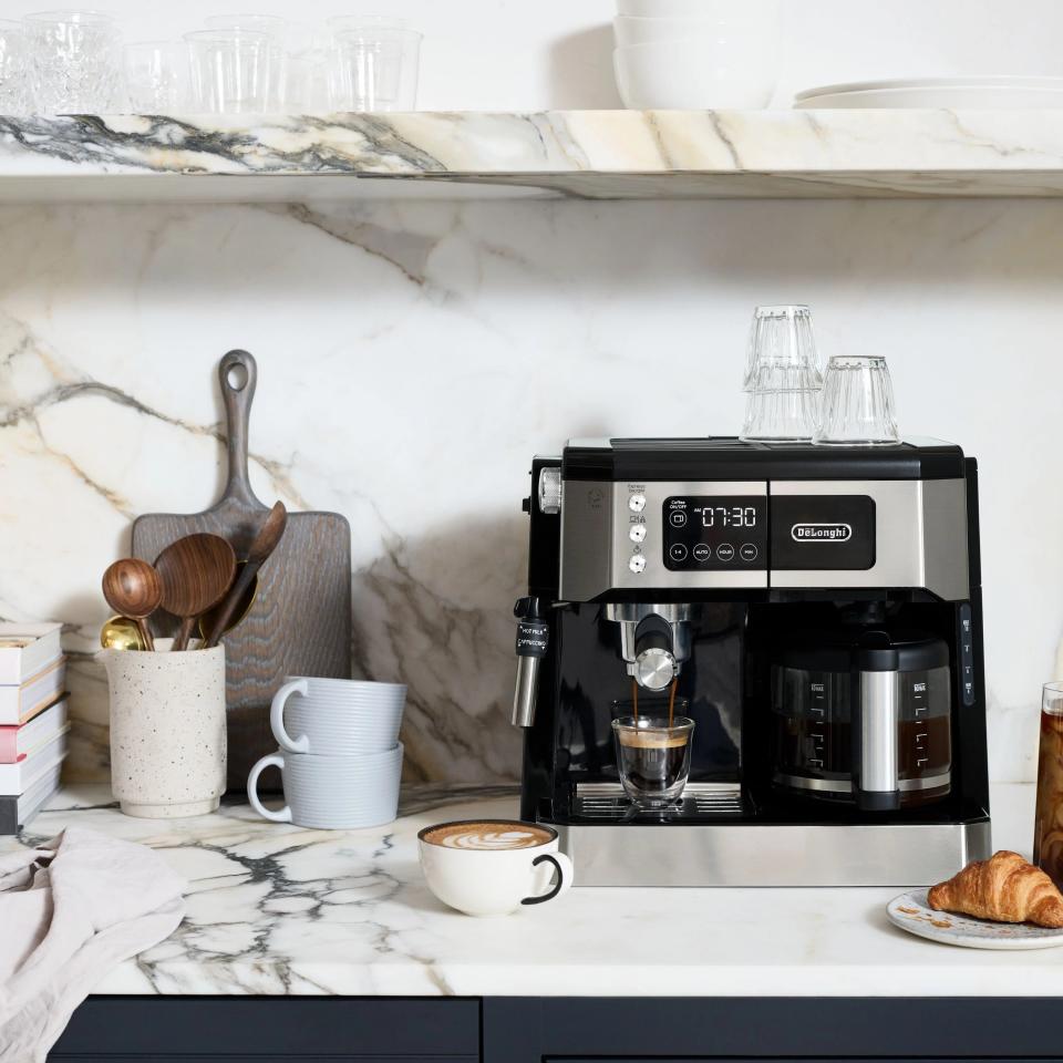 The machine, with a portafilter on the espresso side, a glass carafe on the coffee side, and a frothing wand