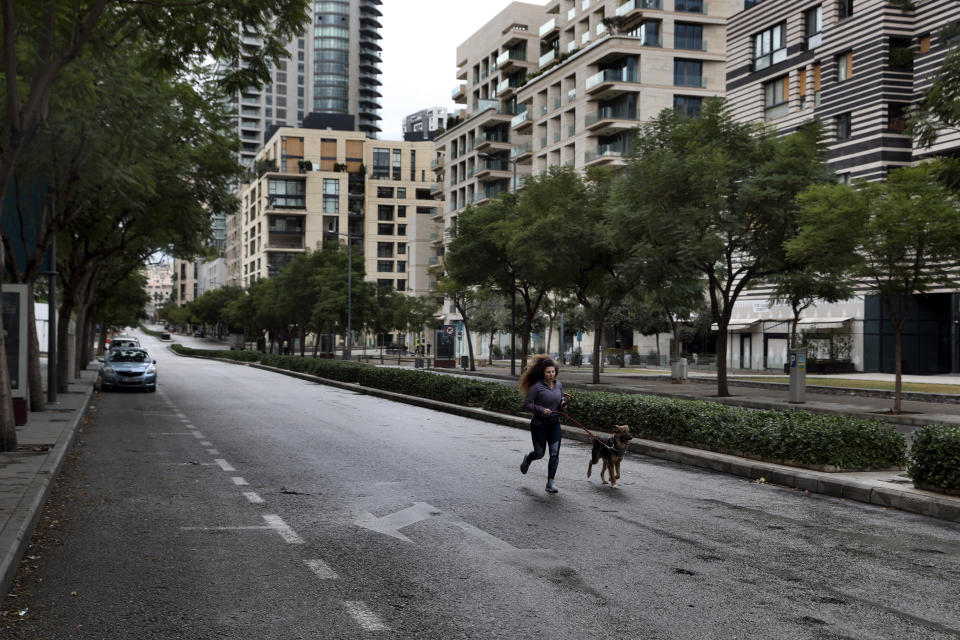 A woman runs with her dog in an almost empty street during a lockdown aimed at curbing the spread of the coronavirus, in Beirut, Lebanon, Thursday, Jan. 14, 2021. Lebanese authorities began enforcing an 11-day nationwide shutdown and round the clock curfew Thursday, hoping to limit the spread of coronavirus infections spinning out of control after the holiday period. (AP Photo/Bilal Hussein)