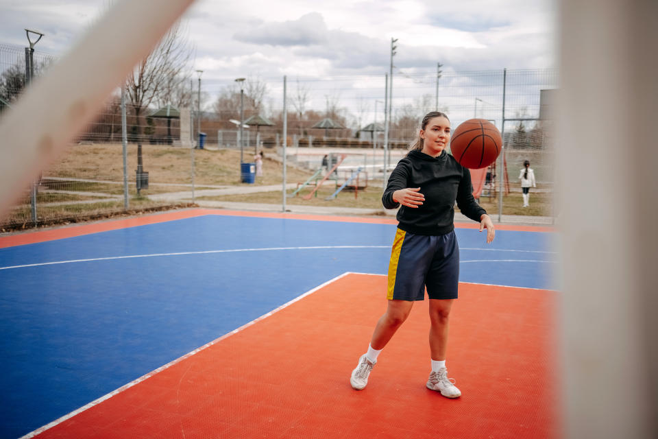 Person playing basketball on an outdoor court, dribbling the ball, wearing athletic attire