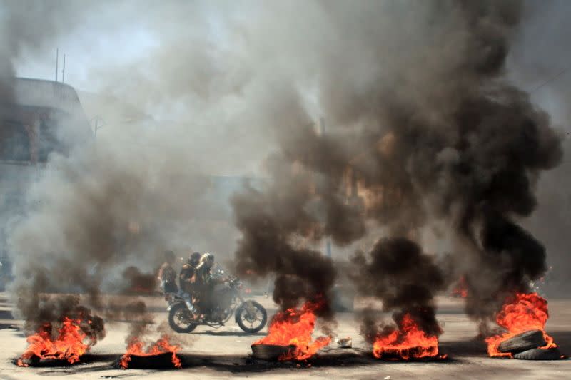 People ride a motorcycle past burning tires during protests against the deteriorating economic situation and the devaluation of the local currency, in Taiz