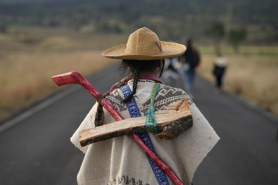 Un indígena purépecha lleva madera y un palo mientras camina con un grupo desde Erongarícuaro, donde los residentes mantuvieron viva una llama durante un año, hasta Ocumicho en el estado de Michoacán, México, el martes 30 de enero de 2024. (AP Foto/Eduardo Verdugo)