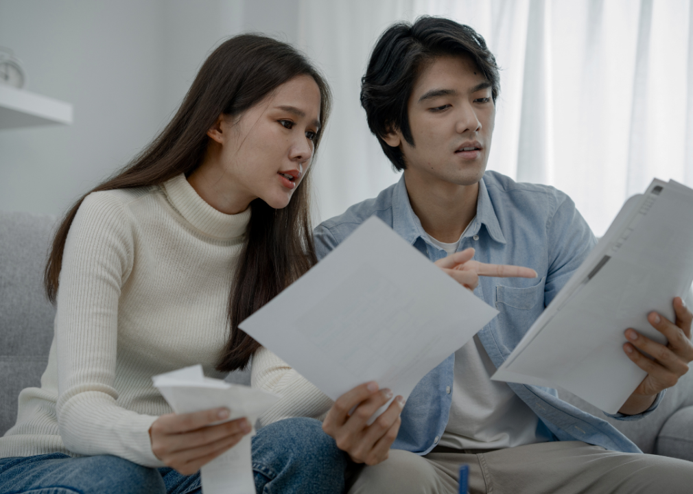 Young, concerned Asian couple looking at the white papers in front of them. 