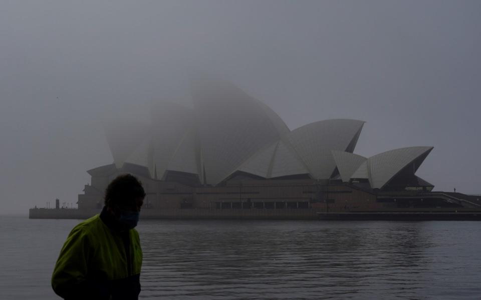 A man wearing a protective face mask walks past the Sydney Opera House, seen shrouded in fog, during a lockdown to curb the spread of a coronavirus disease (COVID-19) outbreak in Sydney, Australia, July 1, 2021. - Reuters