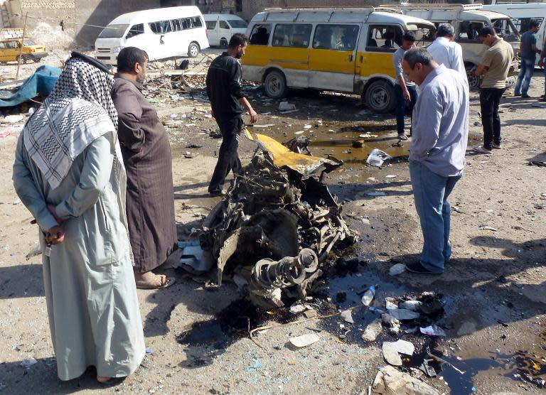 Iraqis look at the remains of a vehicle following an explosion at a bus station on October 27, 2013, in the the Mashtal district of the capital Baghdad