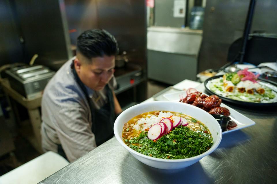 A bowl of spicy birria ramen sits on the counter, alongside other dishes, as resident chef Emilene Carrillo works in the kitchen at Jobot Coffee & Bar on Aug. 4, 2023, in Phoenix.