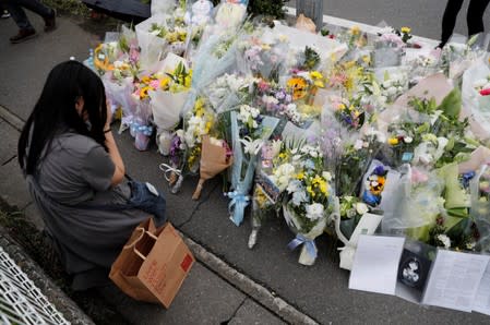 A woman prays in front of a row of flowers placed for victims of the torched Kyoto Animation building in Kyoto