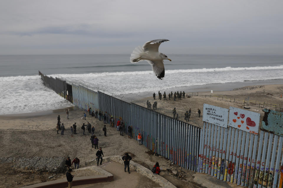 FILE - In this Dec. 10, 2018, file photo, people look on from the Mexican side, left, as U.S. Border Patrol agents on the other side of the U.S. border wall in San Diego prepare for the arrival of hundreds of pro-migration protestors, seen from Tijuana, Mexico. The southern border is nearly 2,000 miles long and already has about 650 miles of different types of barriers, including short vehicle barricades and tall, steel fences that go up to 30 feet high. (AP Photo/Rebecca Blackwell, File)