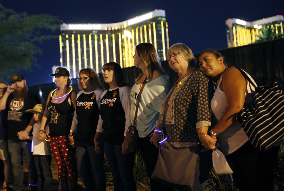 Survivors of a mass shooting form a human chain around the shuttered site of a country music festival on the first anniversary, Monday, Oct. 1, 2018, in Las Vegas. As people were linking arms and holding hands Monday night near the concert site, officials and several hundred others across town listened to bagpipes and the names of the 58 victims being read aloud. (AP Photo/John Locher)