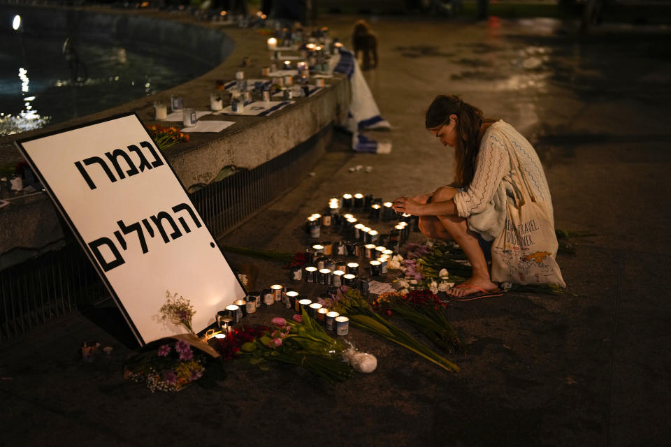A woman lights candles in honor of victims of the Hamas attacks during a vigil at Dizengoff square in central Tel Aviv, Israel, Friday, Oct. 13, 2023. The writing reads: "Out of Words." (AP Photo/Francisco Seco)