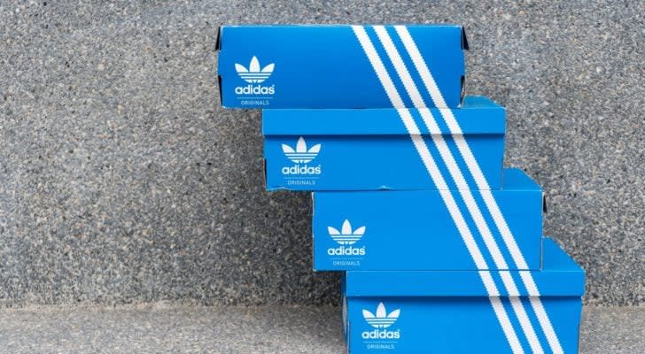 An image of four blue and white Adidas Originals shoe boxes stacked on top of each other with the three white stripes on each box lined up with each other in front of a speckled stone wall.