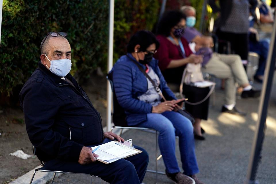 People wait to receive a COVID-19 vaccine at the Families Together of Orange County Community Health Center, Friday, Feb. 26, 2021, in Tustin, Calif. California's governor says a commitment to equity is driving his administration's centralized approach to vaccinating residents. But community health centers say they've watched as initial shipments of the coronavirus vaccine went to larger hospitals, leaving the centers and their high-risk patients to wait.