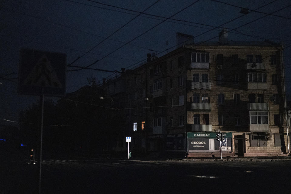A man crosses a pitch-black street in Kharkiv, Ukraine, Sunday, Sept. 11, 2022. The city appeared to be under a complete blackout with no light visible in the city where a fire raged in a power station reportedly hit in a strike. (AP Photo/Leo Correa)