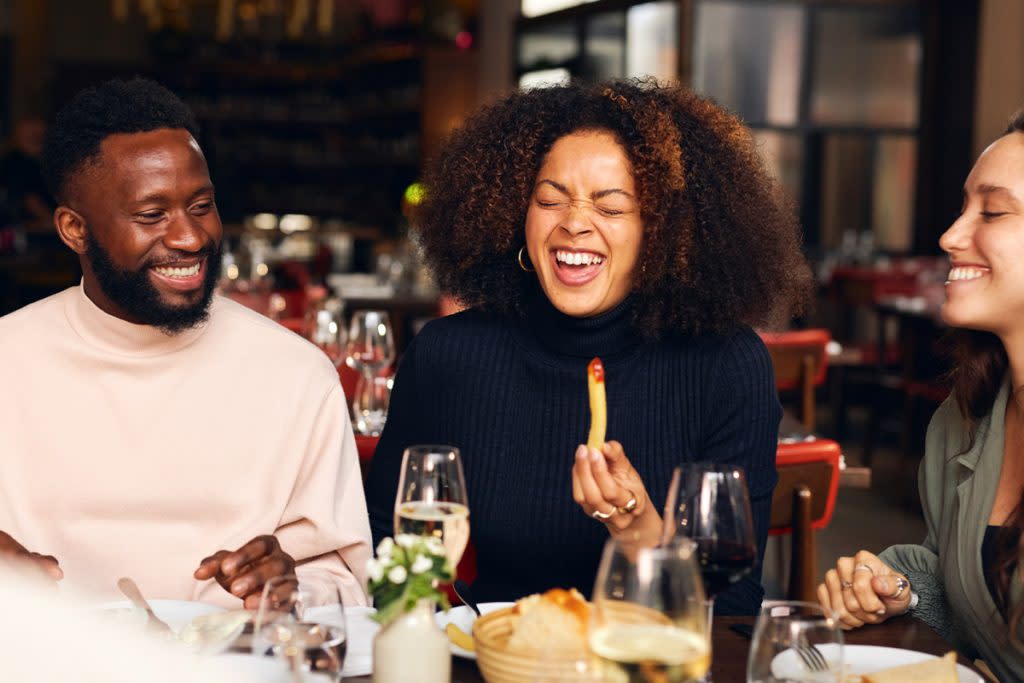 Three people laugh as they eat food at a restaurant.