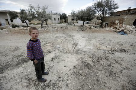 A boy stands near a hole in the ground after a shell fell in the rebel-held town of Jarjanaz, southern Idlib countryside, Syria March 5, 2016. REUTERS/Khalil Ashawi