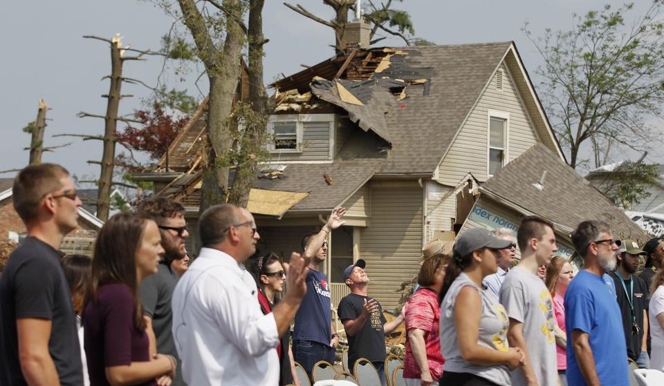 Church members, neighbors, friends and family of the Northridge Wesleyan Church sing during a Sunday service in the parking lot of the tornado damaged church in Harrison Twp. A damaged home on Neff Road is seen in the background.   (WHIO File)