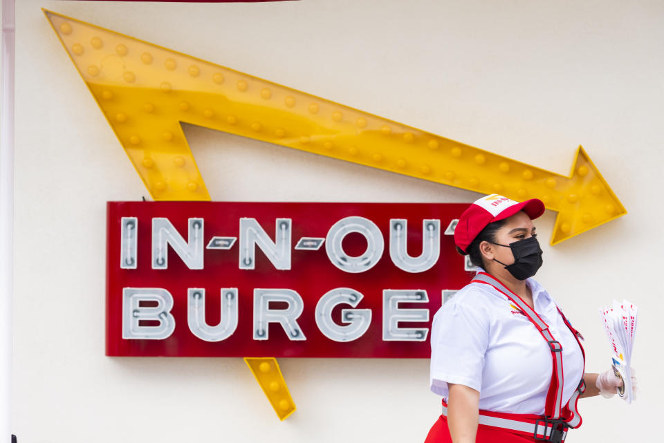 САНТА-АНА, Калифорния - 01 апреля: Сотрудник In-N-Out Burger проходит мимо вывески и нового In-NB-Out на улице Норт-Бристоль в Санта-Ане в четверг, 1 апреля 2021 года. Ресторан открылся после первоначального здания был снесен в 2020 году, чтобы освободить место для нового здания, в котором теперь есть двойные проезды. Первоначальный ресторан мог вместить только около 11 автомобилей, этот новый дизайн вмещает до 34 автомобилей. (Фото Леонарда Ортиса / MediaNews Group / Orange County Register через Getty Images)