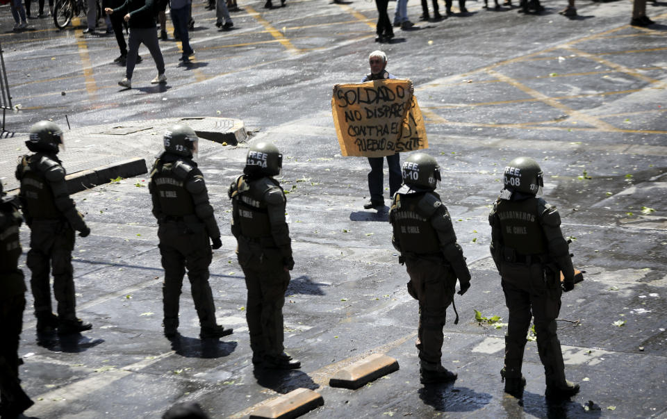 A protester holds a banner that reads in Spanish "Soldier don't fire against the people" in front of riot police during in Santiago, Chile, Wednesday, Oct. 23, 2019. Rioting, arson attacks and violent clashes wracked Chile as the government raised the death toll to 15 in an upheaval that has almost paralyzed the South American country long seen as the region's oasis of stability. (AP Photo/Rodrigo Abd)