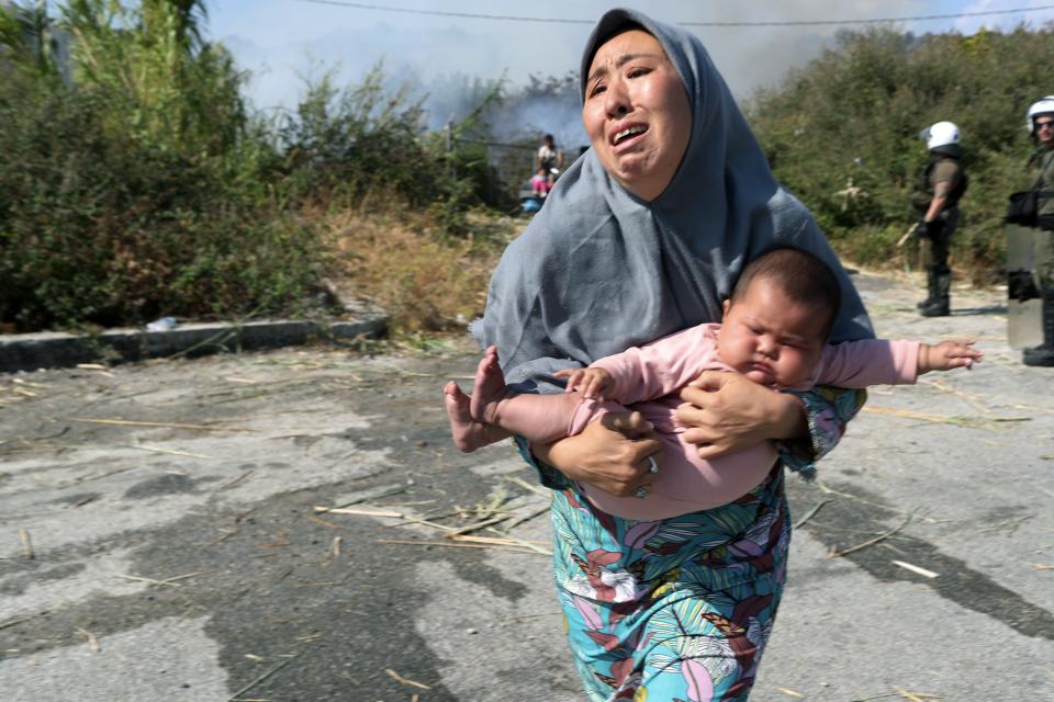 A migrant holds her baby as she runs to avoid a small fire in a field near Mytilene town, on the northeastern island of Lesbos, Greece, Saturday, Sept. 12, 2020. Thousands of asylum-seekers spent a fourth night sleeping in the open on the Greek island of Lesbos, after successive fires destroyed the notoriously overcrowded Moria camp during a coronavirus lockdown. (AP Photo/Petros Giannakouris)