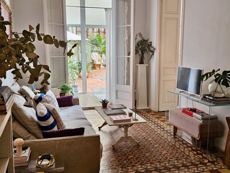 Sofa, stone coffee table with books and candles across from the glass table with TV and plant on it.