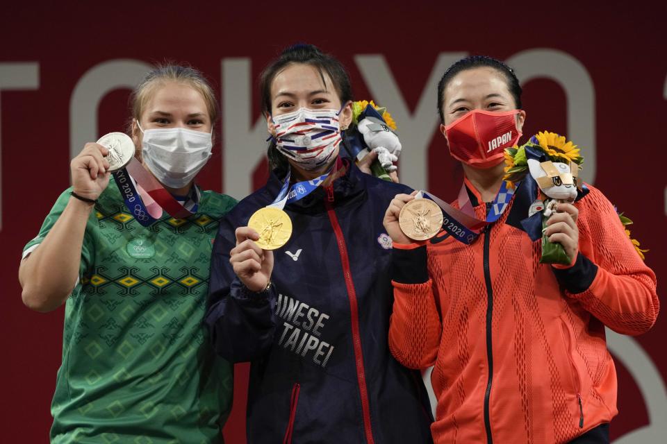 Gold medalist Kuo Hsing-Chun of Taiwan, center, is flanked by silver medalist Polina Guryeva of Turkmekistan, left and bronze medalist Mikiko Andoh of Japan on the podium after the women's 59kg weightlifting event, at the 2020 Summer Olympics, Tuesday, July 27, 2021, in Tokyo, Japan. (AP Photo/Luca Bruno)