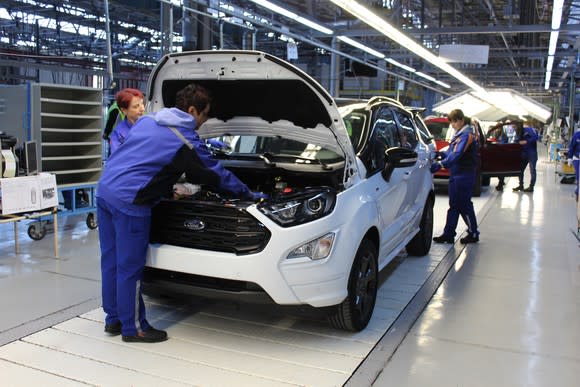 Workers attend to a white Ford EcoSport, a small SUV, on a factory assembly line.